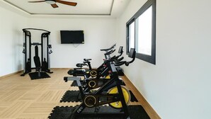 Een fitnessruimte met trainingsfietsen, een plafondventilator, een televisie en een raam.