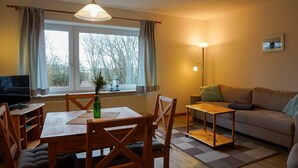 A living room with a sofa, a dining table with chairs, a TV, a lamp, and a window with curtains.