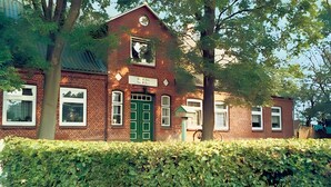 A red brick building with a green door, white windows, and a clock on the wall.