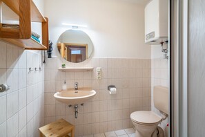 Ein Badezimmer mit Waschbecken, Toilette und einem Holzregal darüber.