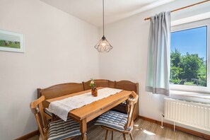 Ein Essbereich mit Holztisch, Stühlen, einer Pendelleuchte, einem Fenster mit Vorhängen und einer Heizung.