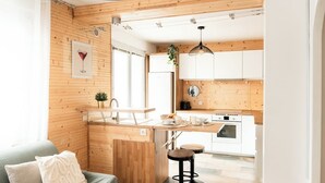 Ett modernt kök med träväggar, en matplats med barstolar och ett vardagsrum med en soffa.