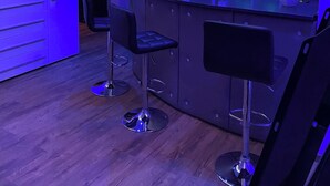 Un espace bar moderne comprenant un comptoir, deux tabourets et un réfrigérateur portant l’inscription « VIO ».