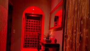 Un couloir avec une porte illuminée de rouge, des meubles en bois et un miroir au mur.
