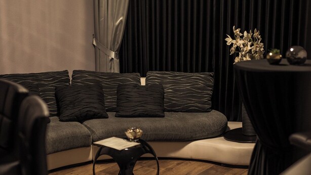 Un salon moderne avec un canapé gris, des coussins noirs, une petite table d’appoint ronde et une autre table plus petite sur laquelle sont disposés des objets décoratifs.