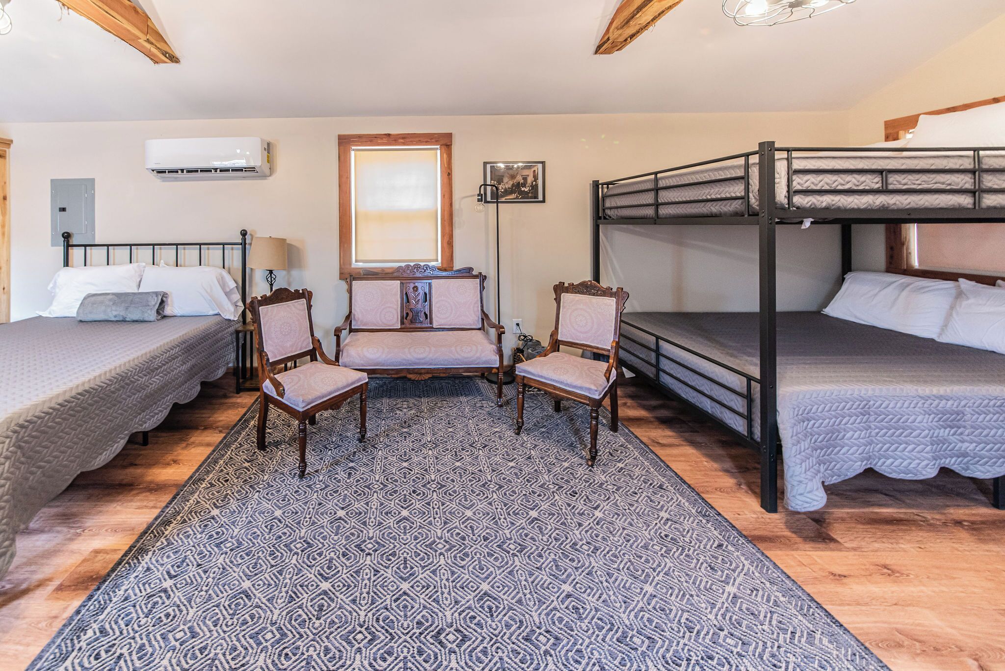 A room with two single beds, a bunk bed, a patterned rug, and two wooden chairs.