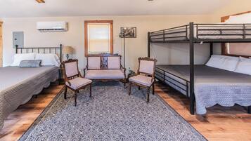 A room with two single beds, a bunk bed, a patterned rug, and two wooden chairs.