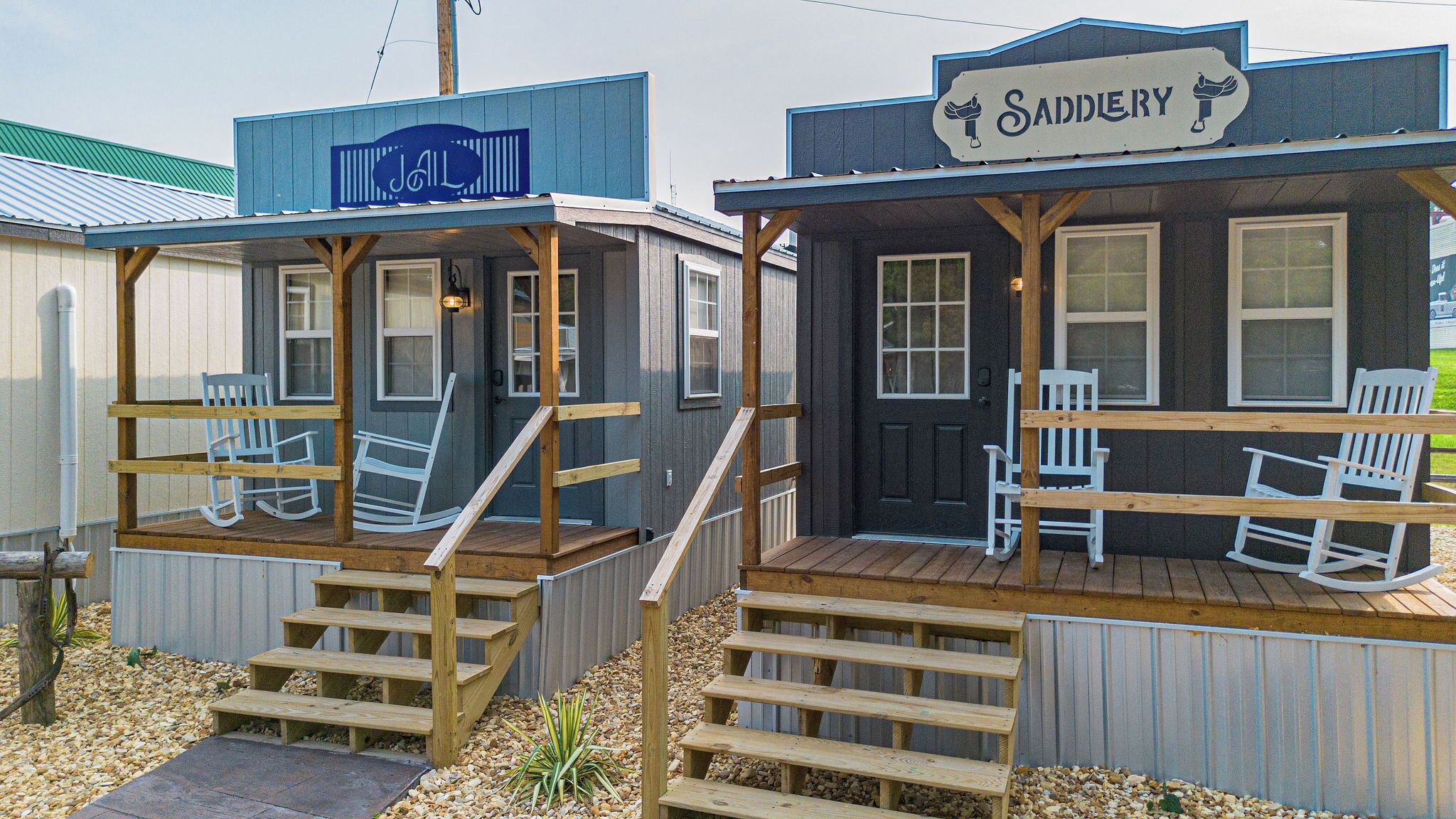 Two small cabins with wooden decks and rocking chairs, each with a sign indicating a different name.