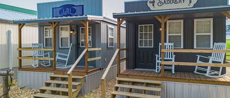 Two small cabins with wooden decks and rocking chairs, each with a sign indicating a different name.