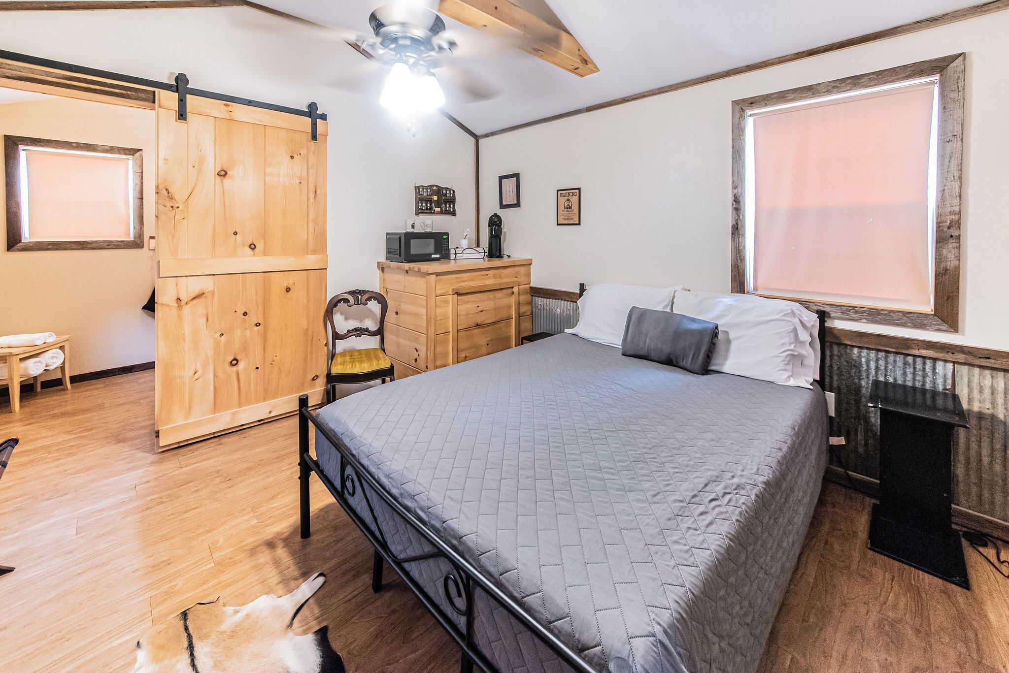 A bedroom with a bed, wooden wardrobe, a desk with a computer, a chair, and a dog.