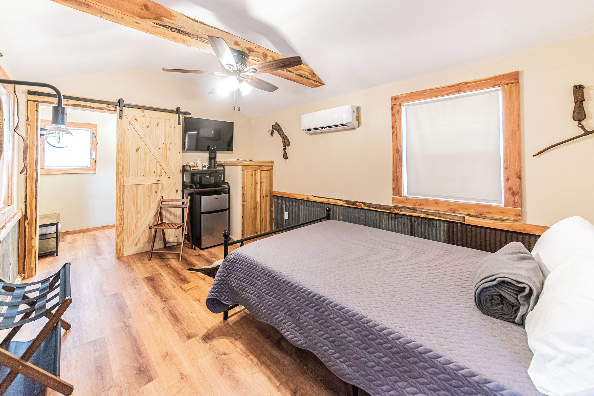 A room with a bed, a desk, a chair, a ceiling fan, an air conditioning unit, and a television.