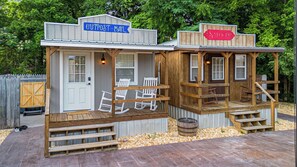 A rustic cabin-style building with a porch, two rocking chairs, and a wooden barrel.