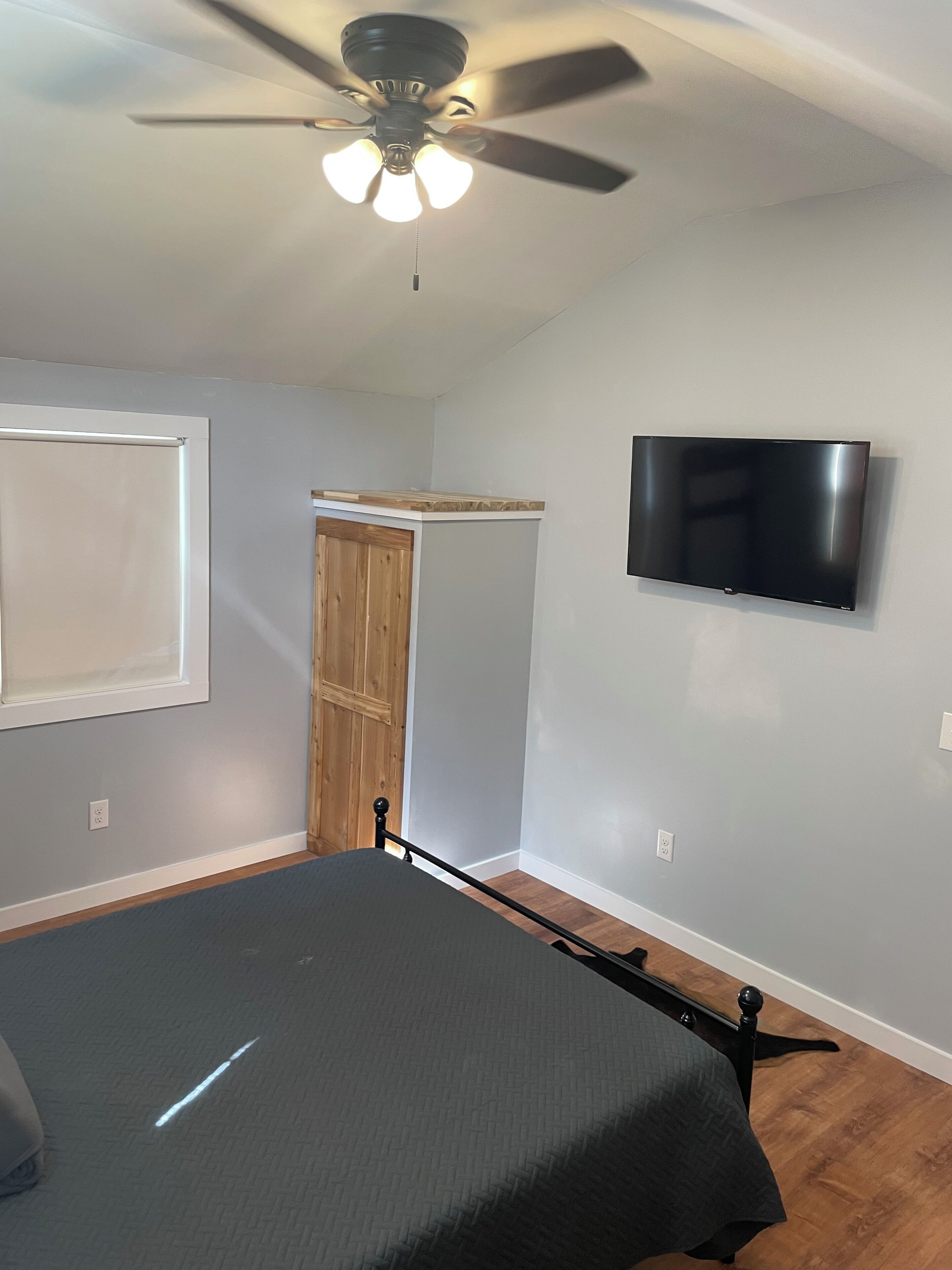 Une chambre à coucher avec un lit, un ventilateur de plafond, une télévision et une armoire en bois.