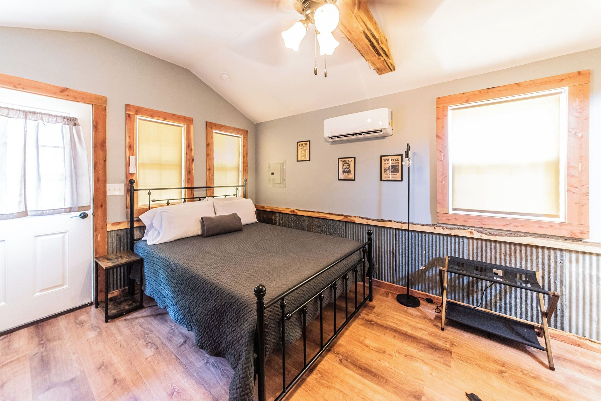 A bedroom with a bed, wooden floor, a ceiling fan, and a window.