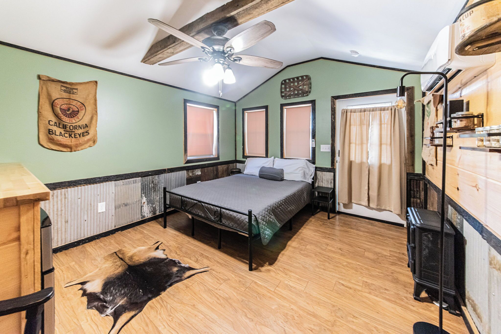 Una habitación con cama, ventilador de techo, radiador, ventana y alfombra de piel.