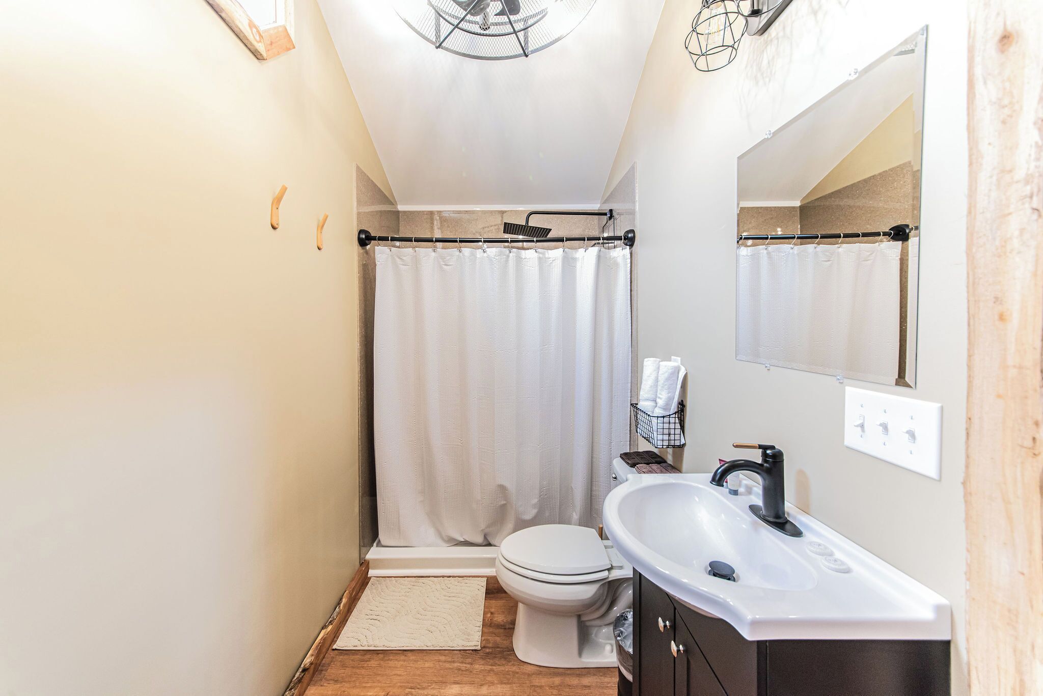 A compact bathroom with a white toilet, a shower curtain, a sink, and a mirror.