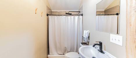 Un baño pequeño con inodoro blanco, cortina de ducha, lavamanos y espejo.