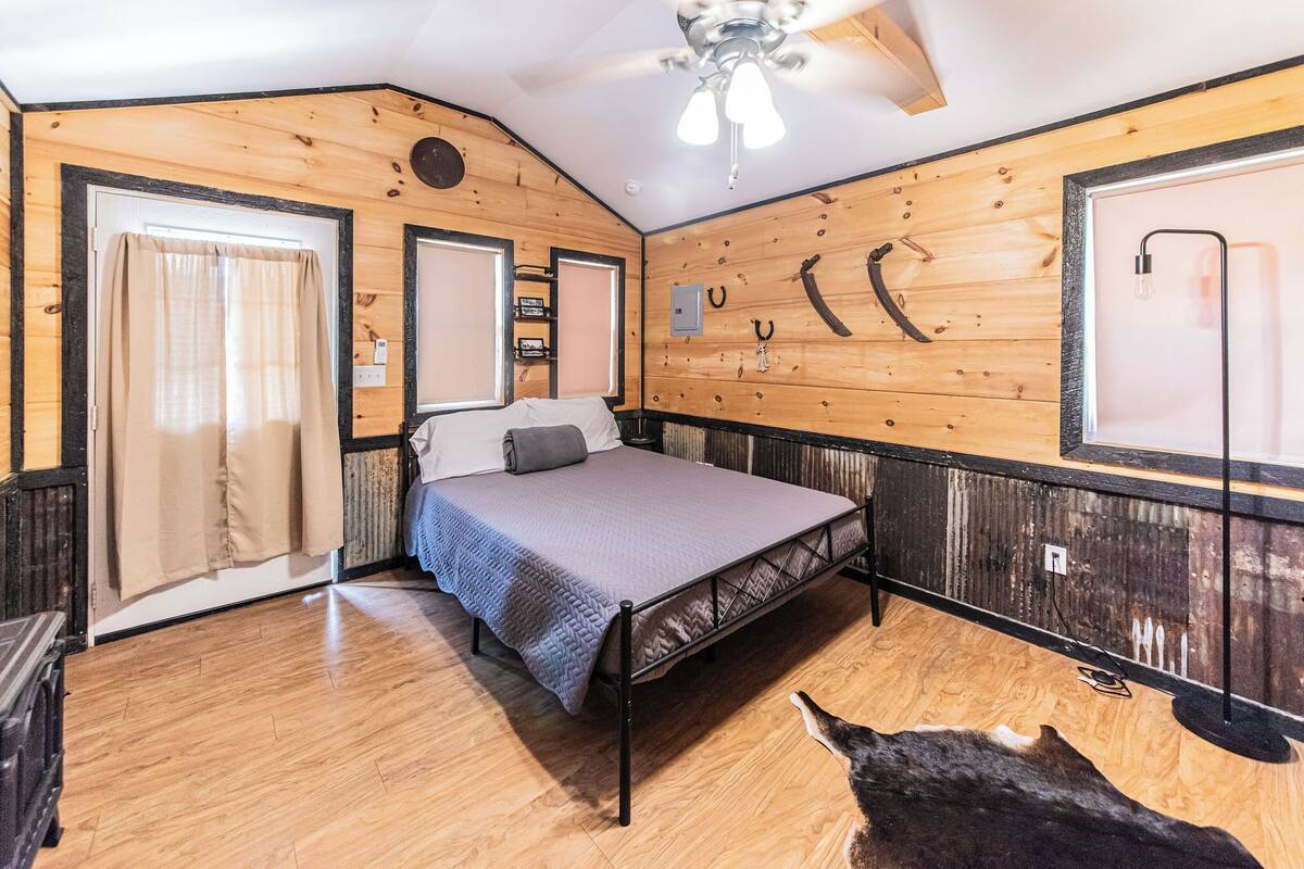 A bedroom with a bed, wooden walls, a ceiling fan, and a window with curtains.