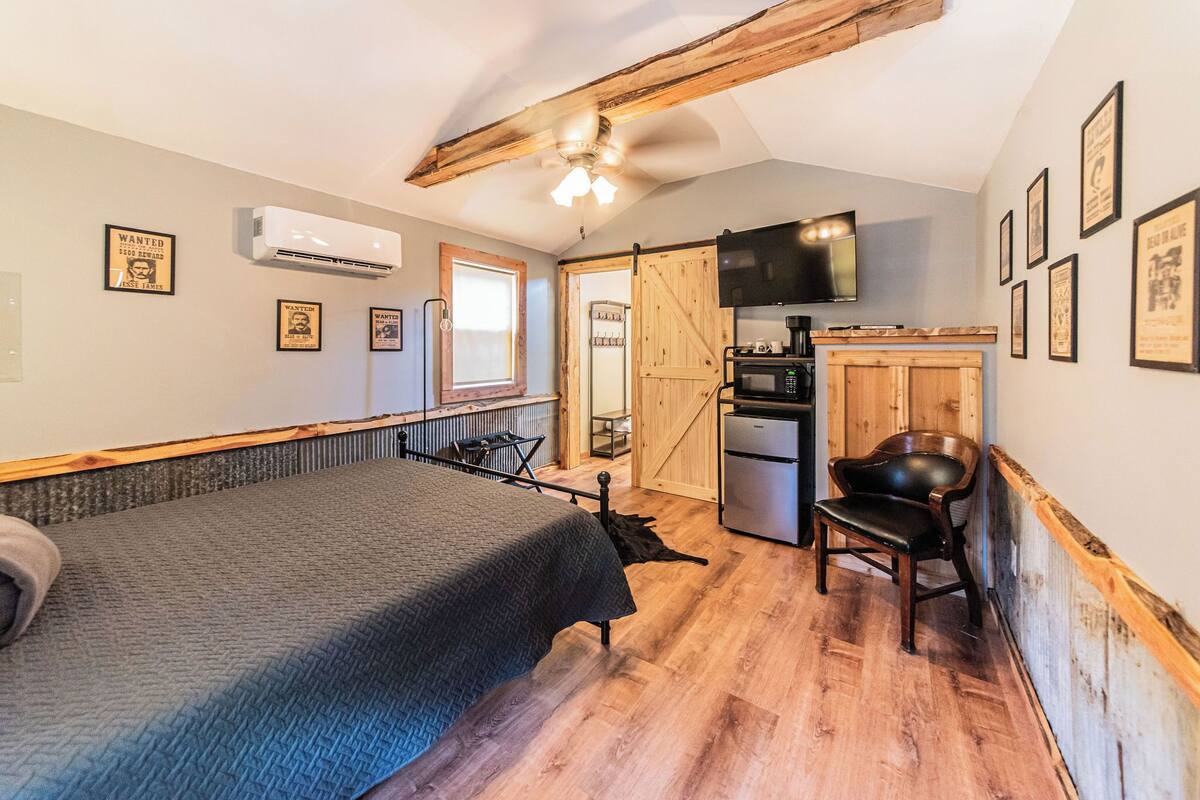 A compact room with a bed, a kitchenette, a TV, and a wooden ceiling.