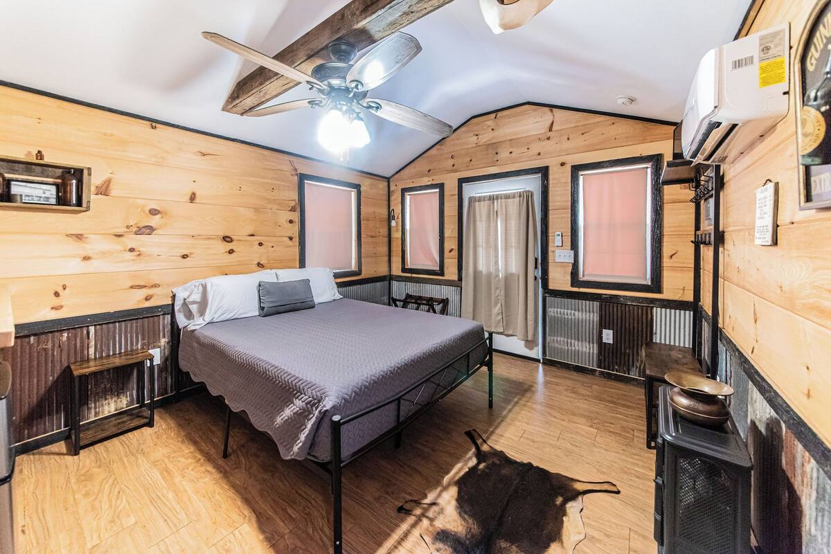 A wooden cabin-style room with a bed, a ceiling fan, a heater, and a rustic decor.