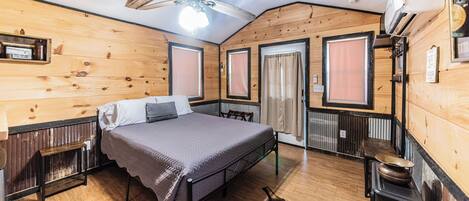 Una habitación tipo cabaña de madera con cama, ventilador de techo, calefacción y decoración rústica.