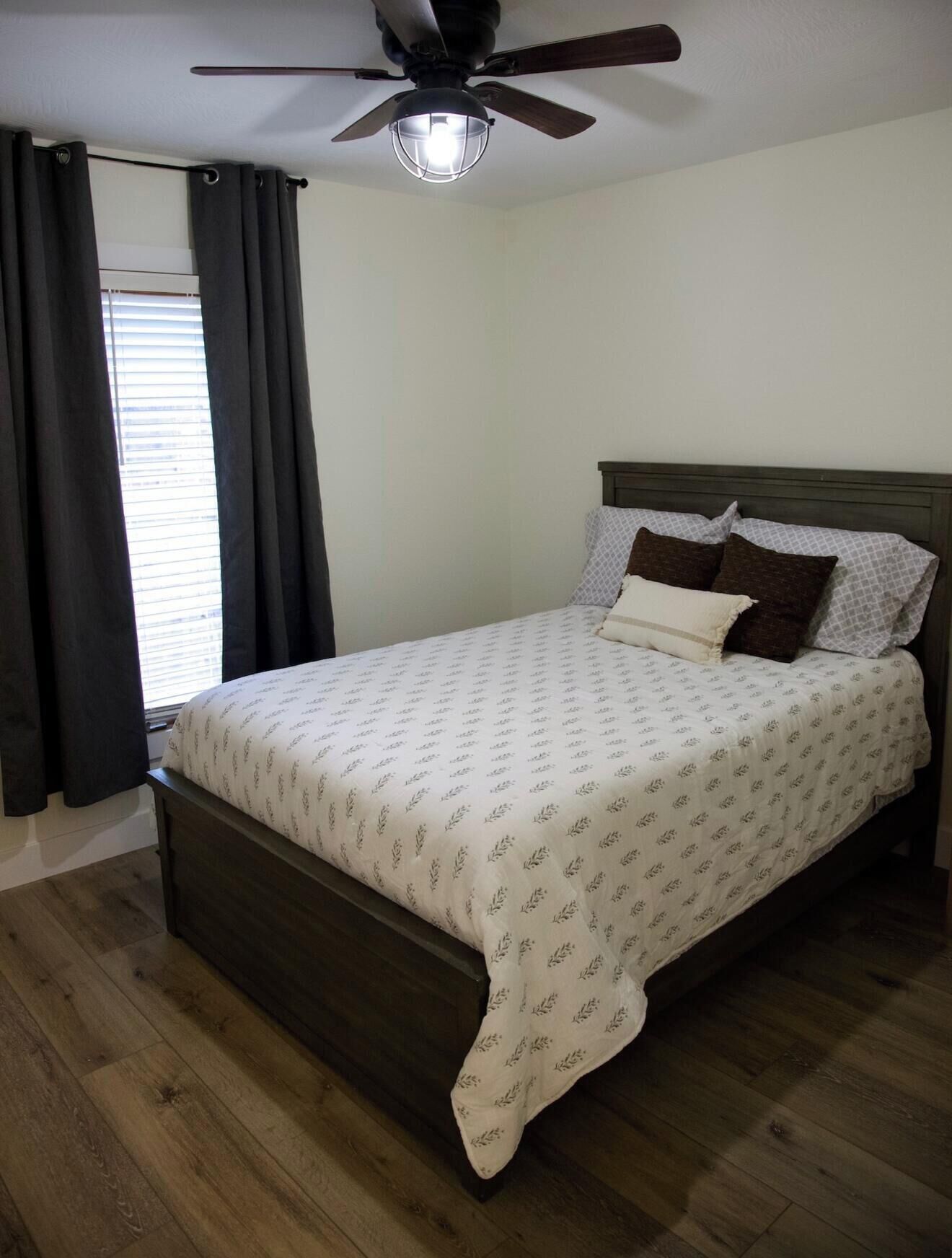 Une chambre à coucher avec un lit, une tête de lit en bois foncé et un ventilateur de plafond.