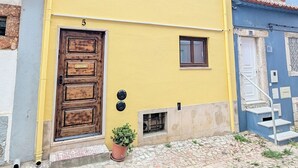 Ein gelbes Gebäude mit einer braunen Tür, einem kleinen Fenster und einem Blumentopf davor.
