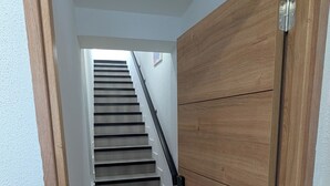 Eine holzrahmenverkleidete Tür führt zu einer Treppe, an einer weißen Wand mit einer weiteren Holztür.