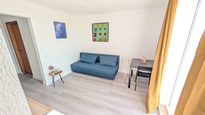 Ein Wohnzimmer mit einem blauen Sofa, einem kleinen Tisch mit einer Vase und einem Gemälde an der Wand.