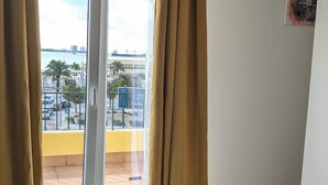 Ein Zimmer mit einer Schiebeglastür zu einem Außenbereich, einem kleinen Holzregal und einem an der Wand befestigten Bild.