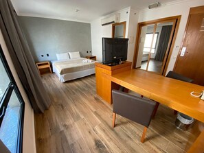 A hotel room with a bed, a desk with a chair, a television, and a large mirror.