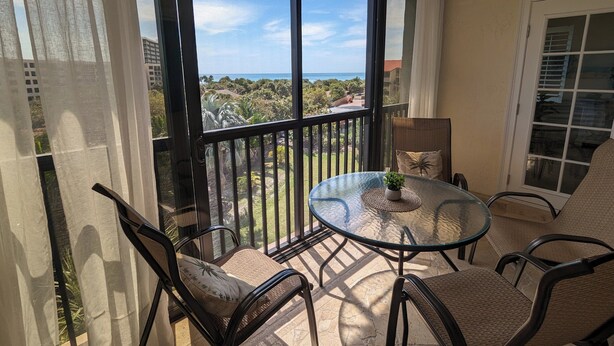Ein Balkon mit Glastisch und Stühlen, Blick aufs Meer und eine Tür rechts.