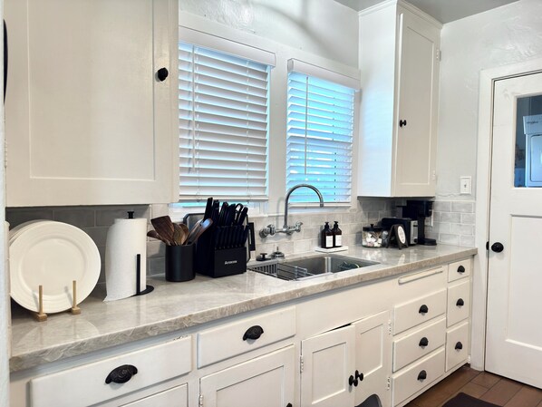 A kitchen with white cabinets, a sink, and a window with blinds.