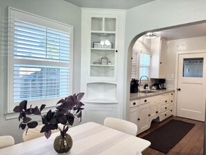 A kitchen with white cabinetry, a built-in oven, and a dining area with a table and chairs.