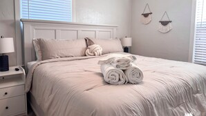 Ein ordentlich bezogenes Bett mit aufgerollten Handtüchern, einer Nachttischlampe und einem Nachttisch.