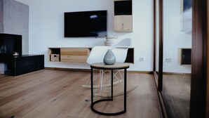 A modern living room with a wooden floor, a round table with a vase, a flat-screen TV mounted on the wall, and a wooden bench with storage. - Apart Veronika - Exclusive living in Imst (Gemeinde Imst)