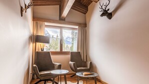 Una habitación con dos sillones de cuero, una mesita redonda, un manto de piel, suelo de madera, una ventana con cortinas y una cabeza de ciervo montada en la pared.