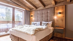 Un dormitorio con una cama grande, vigas de techo de madera, una mesita de noche y vistas a las montañas a través de una puerta corredera.