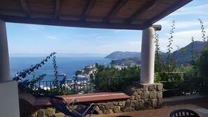 Un espace extérieur abrité, aménagé pour s’asseoir, avec vue sur la mer et une montagne.