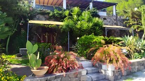 Une maison avec une façade en pierre, un patio couvert et une grande variété de plantes.