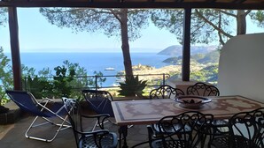 A covered outdoor seating area with a table and chairs, overlooking a coastal landscape with a view of the sea and distant hills. - Apartment in Villa "Stromboli" with Sea View, Wi-Fi and Air Conditioning (Lipari)