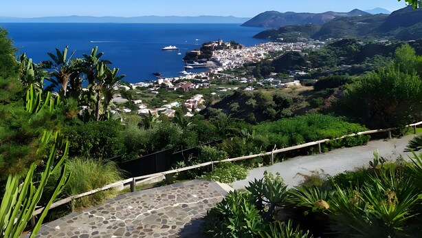 A coastal town with a stone pathway, lush greenery, and a view of the sea and distant mountains. - Apartment in Villa "Stromboli" with Sea View, Wi-Fi and Air Conditioning (Lipari)