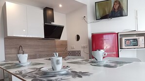 A modern kitchen with white cabinets, a red coffee machine, and a flat-screen TV mounted on the wall. - Terra Nova Casa - Free parking 24/24 (Pau)