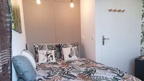 A bedroom with a bed featuring a tropical leaf pattern bedspread, a woven headboard, and two pillows with animal prints. - Terra Nova Casa - Free parking 24/24 (Pau)