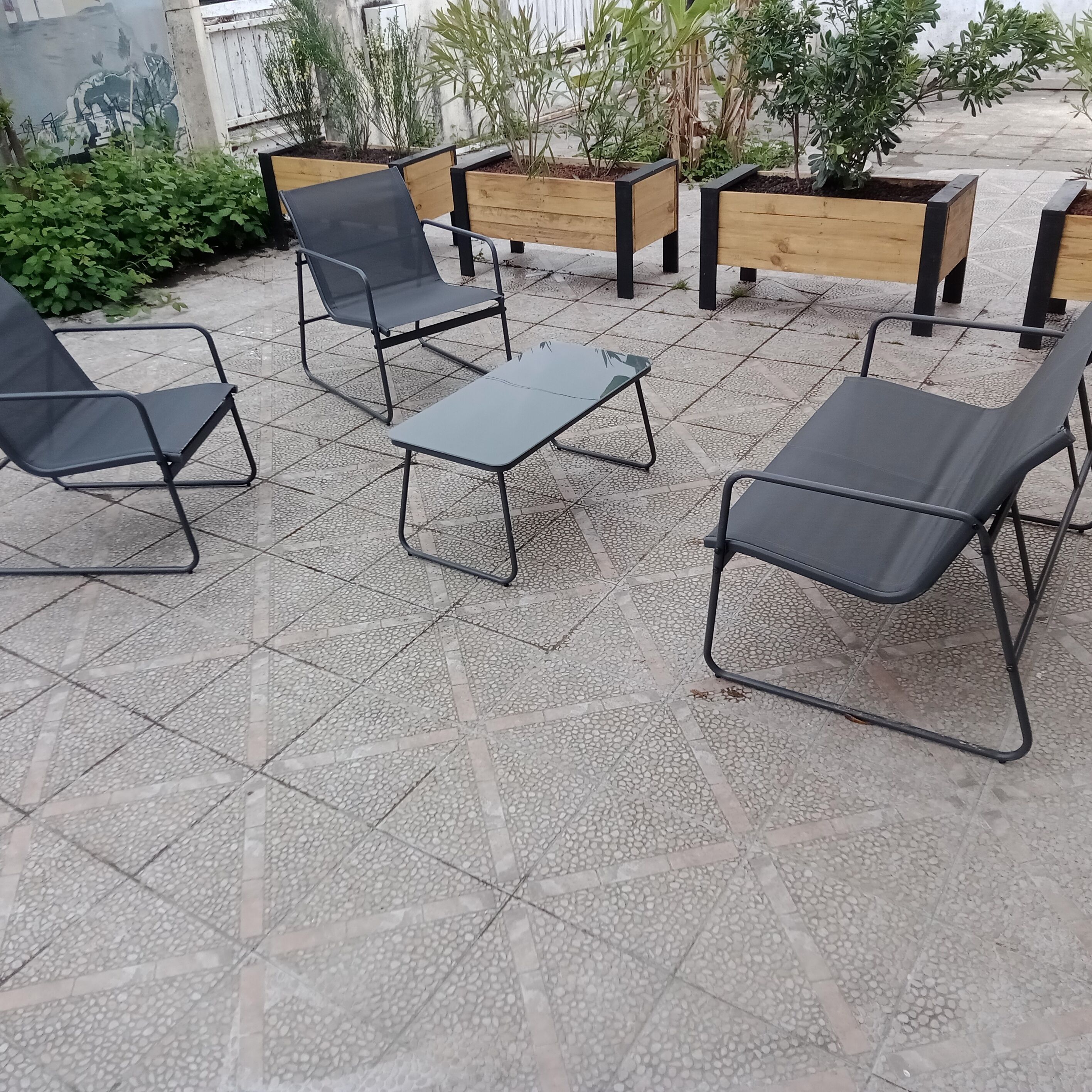 Area esterna con sedute in metallo, sedie e un tavolo, circondata da fioriere con diverse piante.