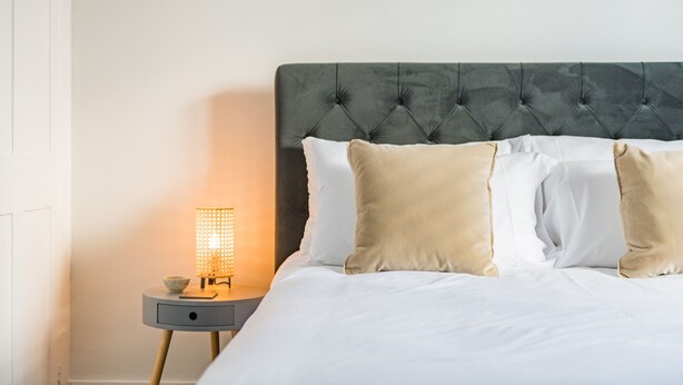 A neatly made bed with a tufted headboard, a bedside table with a lamp, and a bowl. - Penshurst House Deal, Kent (Deal)