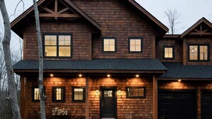 A two-story wooden house with a dark roof, multiple windows, and a front door. - Lux 5BR South Peak Loon - riverfront w swimming and beach - hot tub - pets ok (Lincoln)