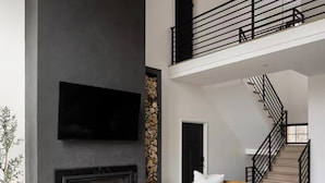 A modern living room with a fireplace, a sofa, a coffee table, and a staircase. - Lux 5BR South Peak Loon - riverfront w swimming and beach - hot tub - pets ok (Lincoln)