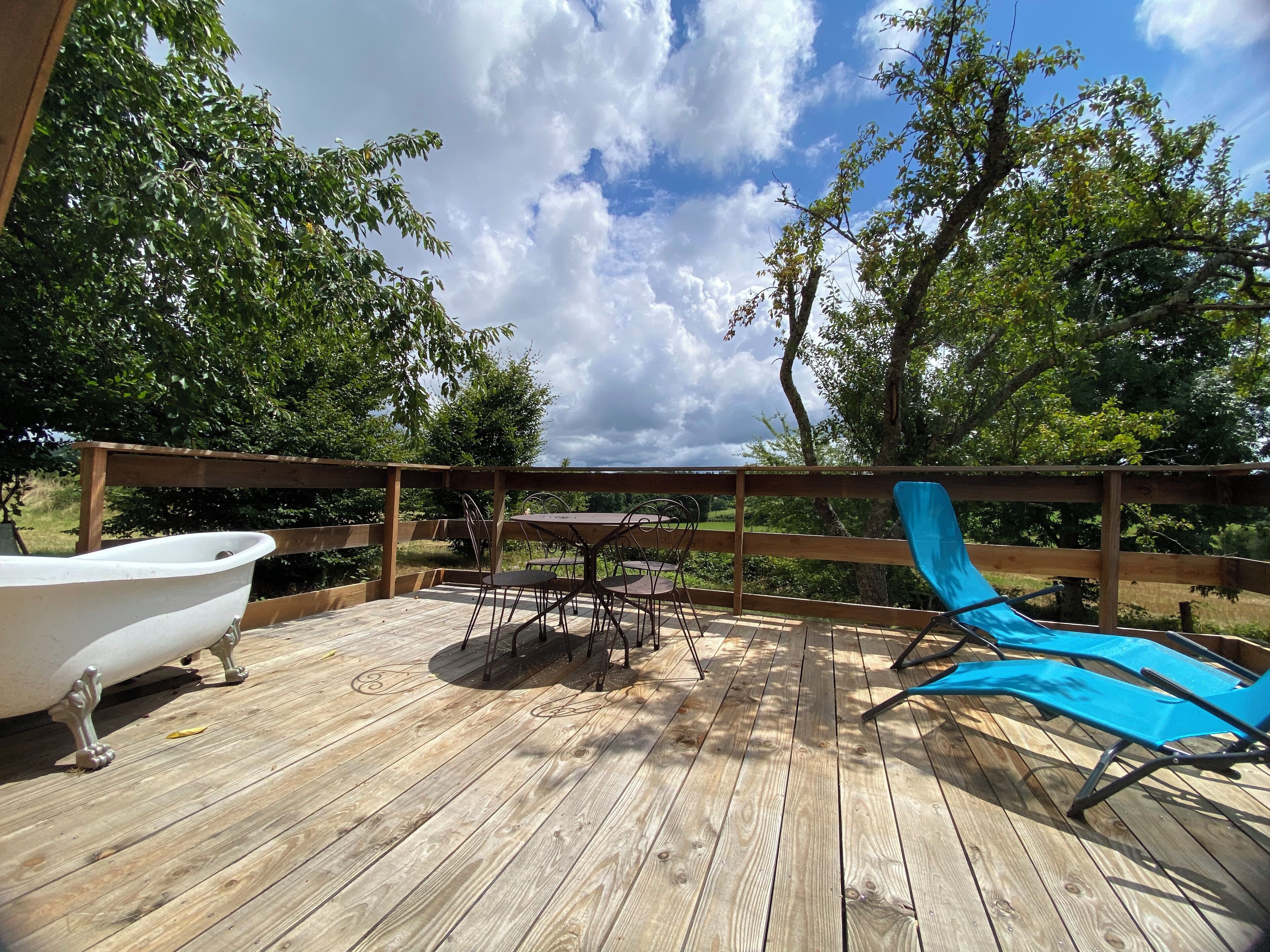 A wooden deck with a table and chairs, a white bathtub, and a blue lounge chair.