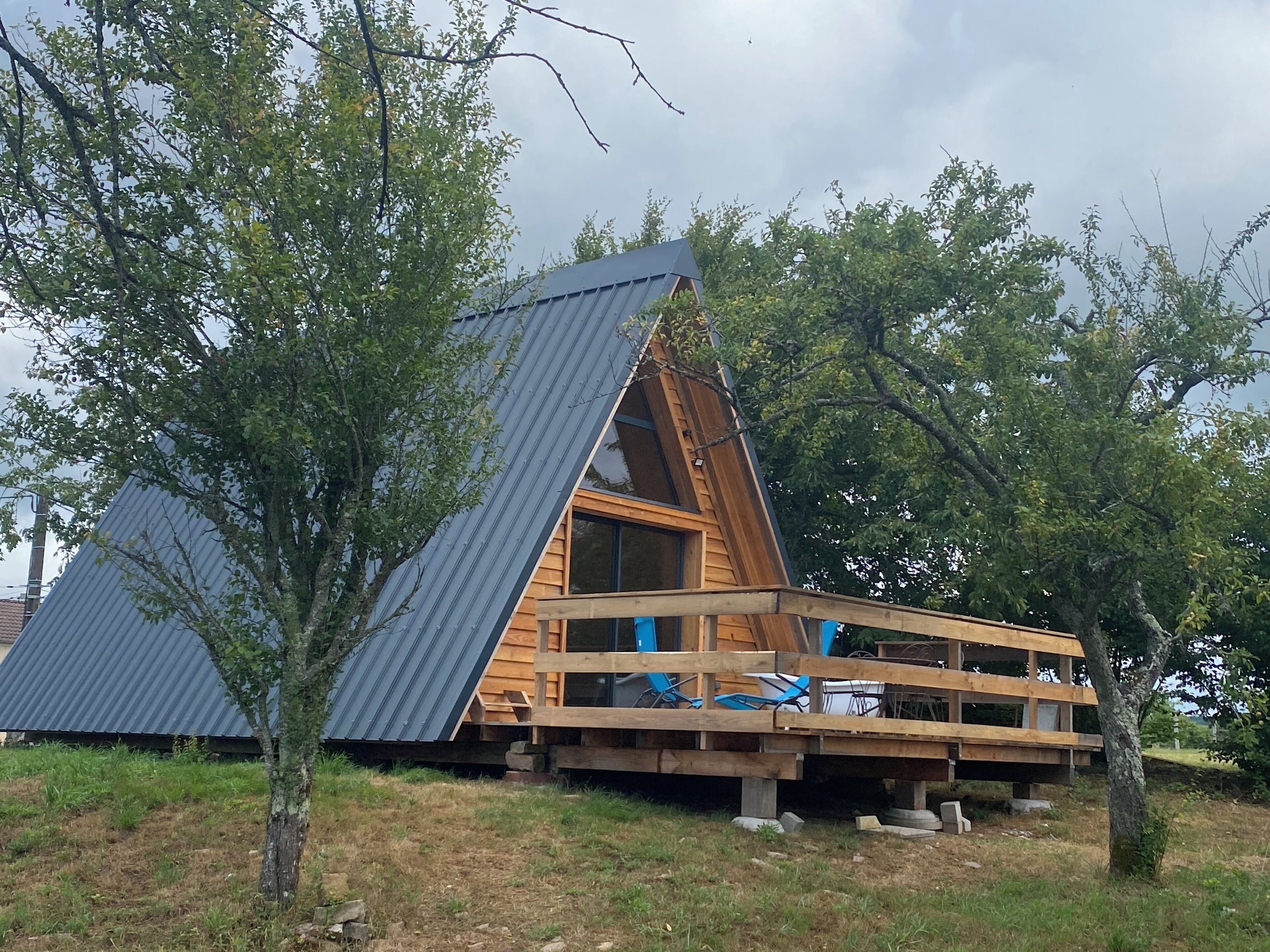 A triangular wooden cabin with a metal roof, surrounded by trees.
